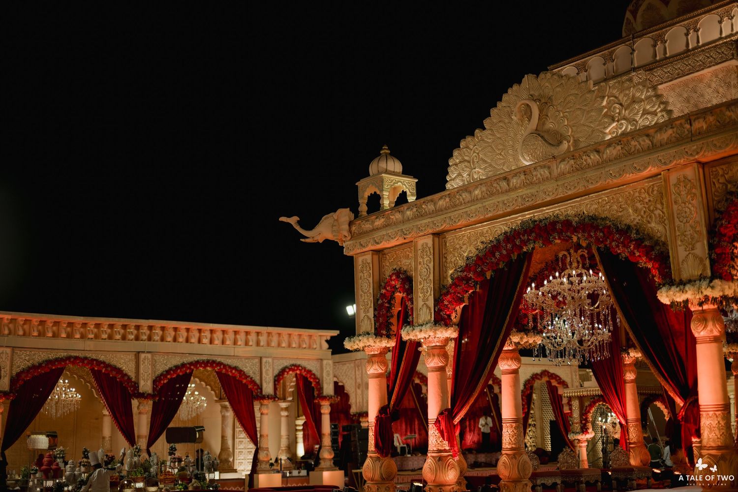 Ornate Indian wedding venue at night with red drapes, chandeliers, and elephant sculpture atop illuminated palace facade.