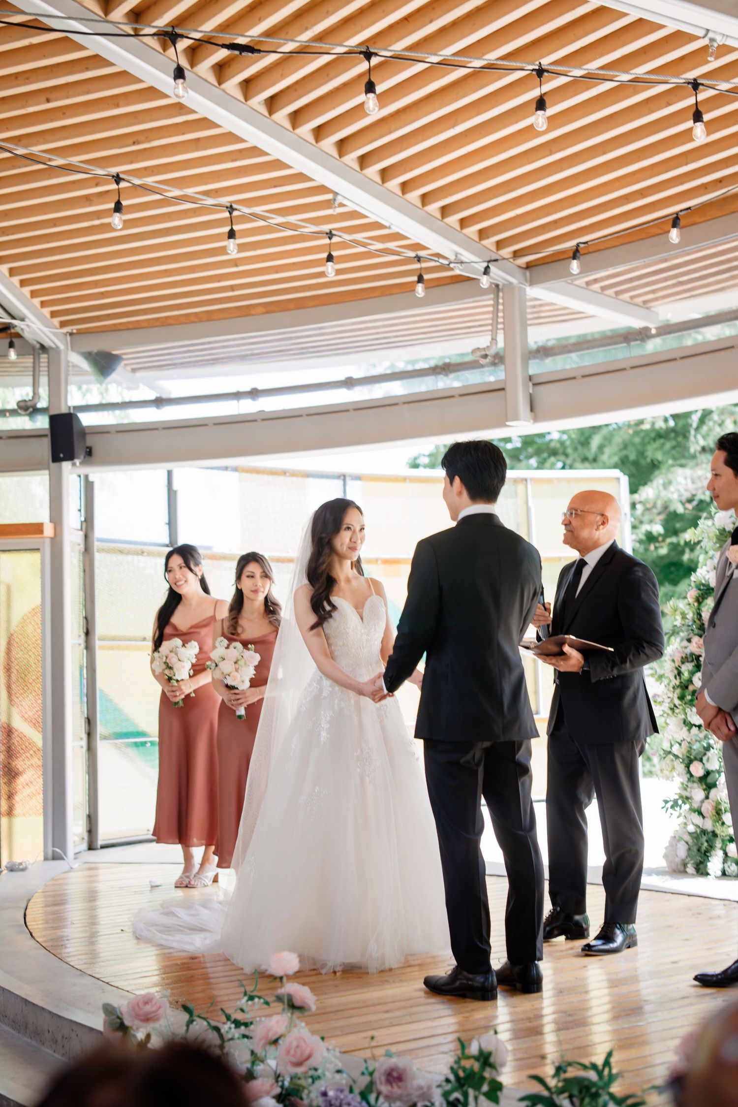 A wedding ceremony takes place in a modern venue with wooden beams and glass walls overlooking a scenic outdoor view.Queen Elizabeth Park We