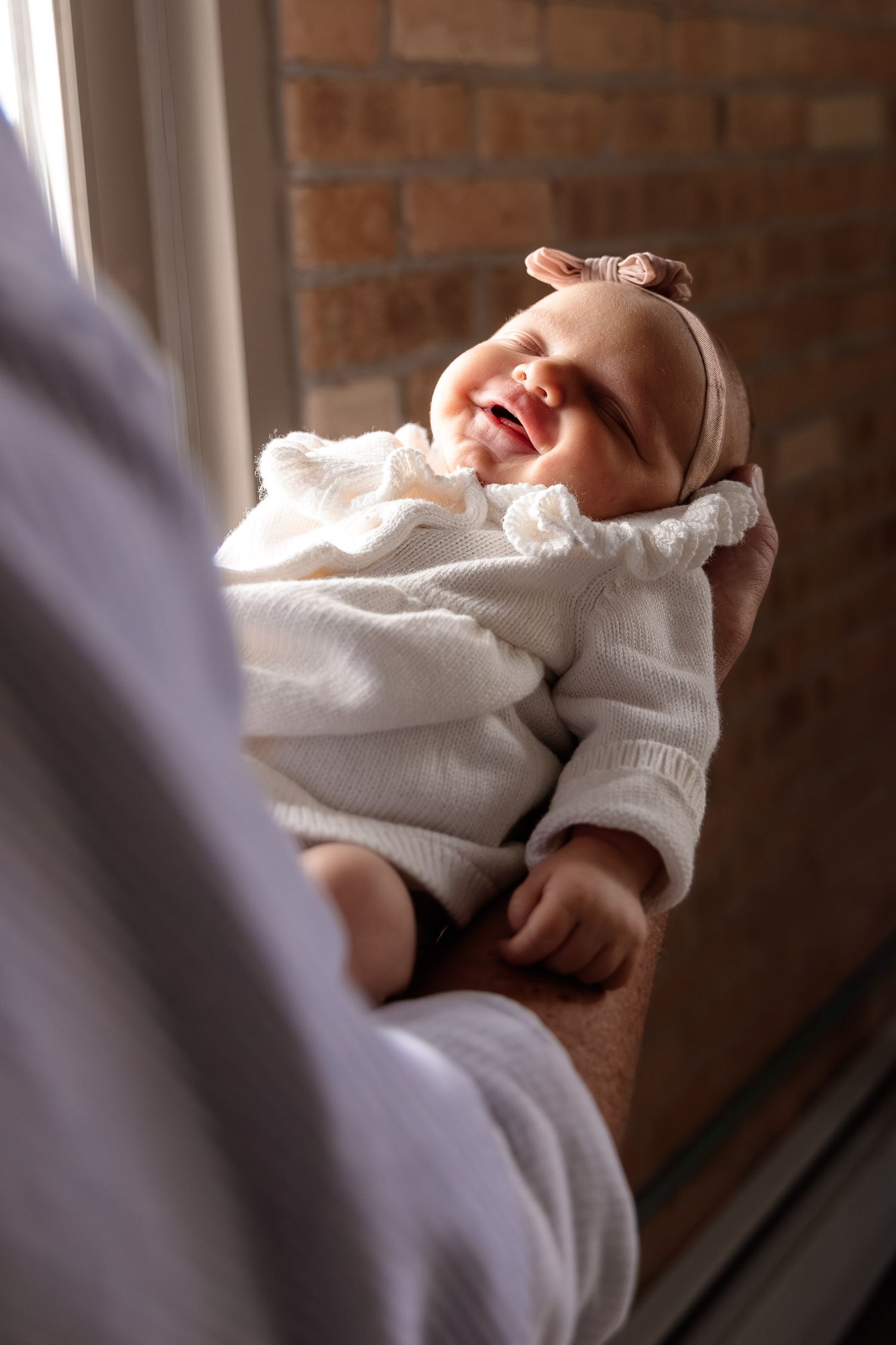 A sleeping baby wearing a white sweater rests peacefully against a brick wall background.