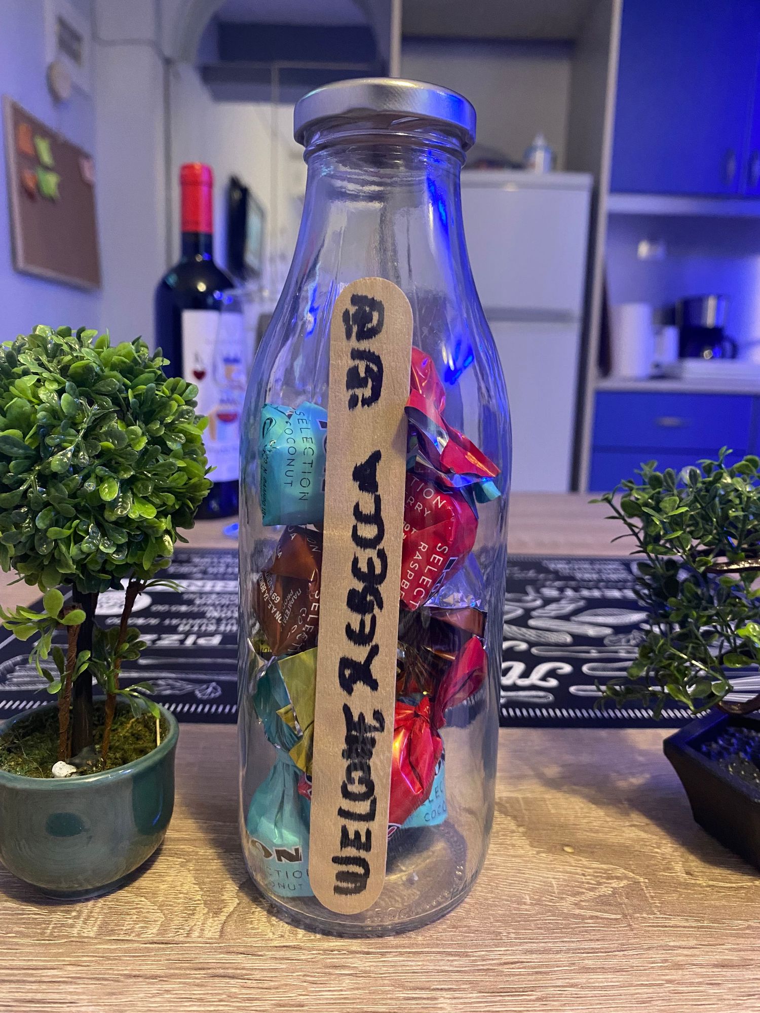 Glass jars with plants and writing sit in a row on a wooden surface with blue lighting in the background.
