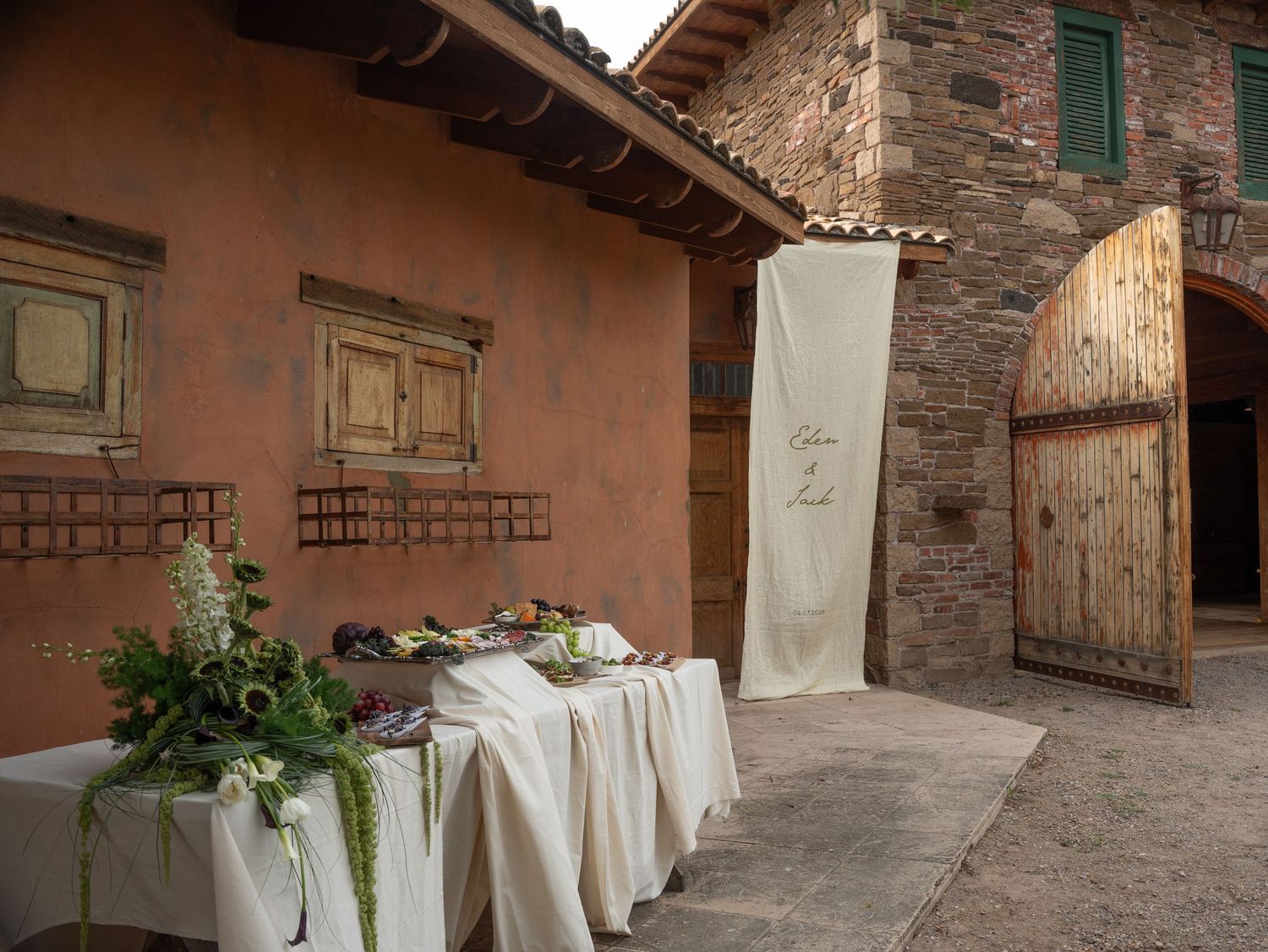 A bride in a white strapless gown holds a lush bouquet of white flowers and greenery while standing by wooden doors.