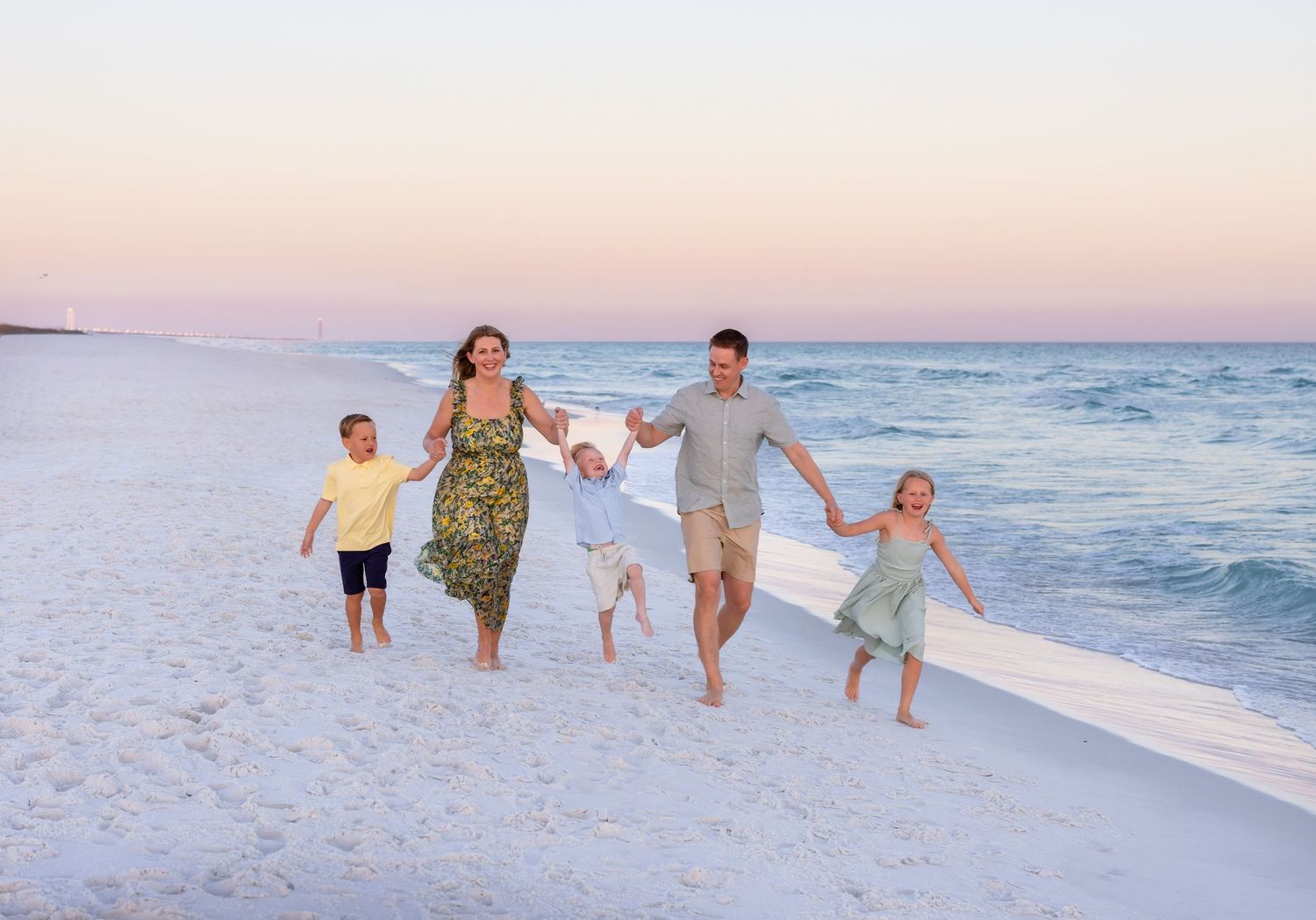 Family enjoying a sunset walk along a pristine white sandy beach with gentle waves in the background.