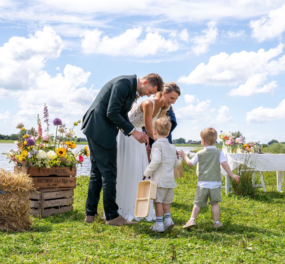 Bride and groom with two young children at an outdoor wedding ceremony with floral arrangements on hay bales.