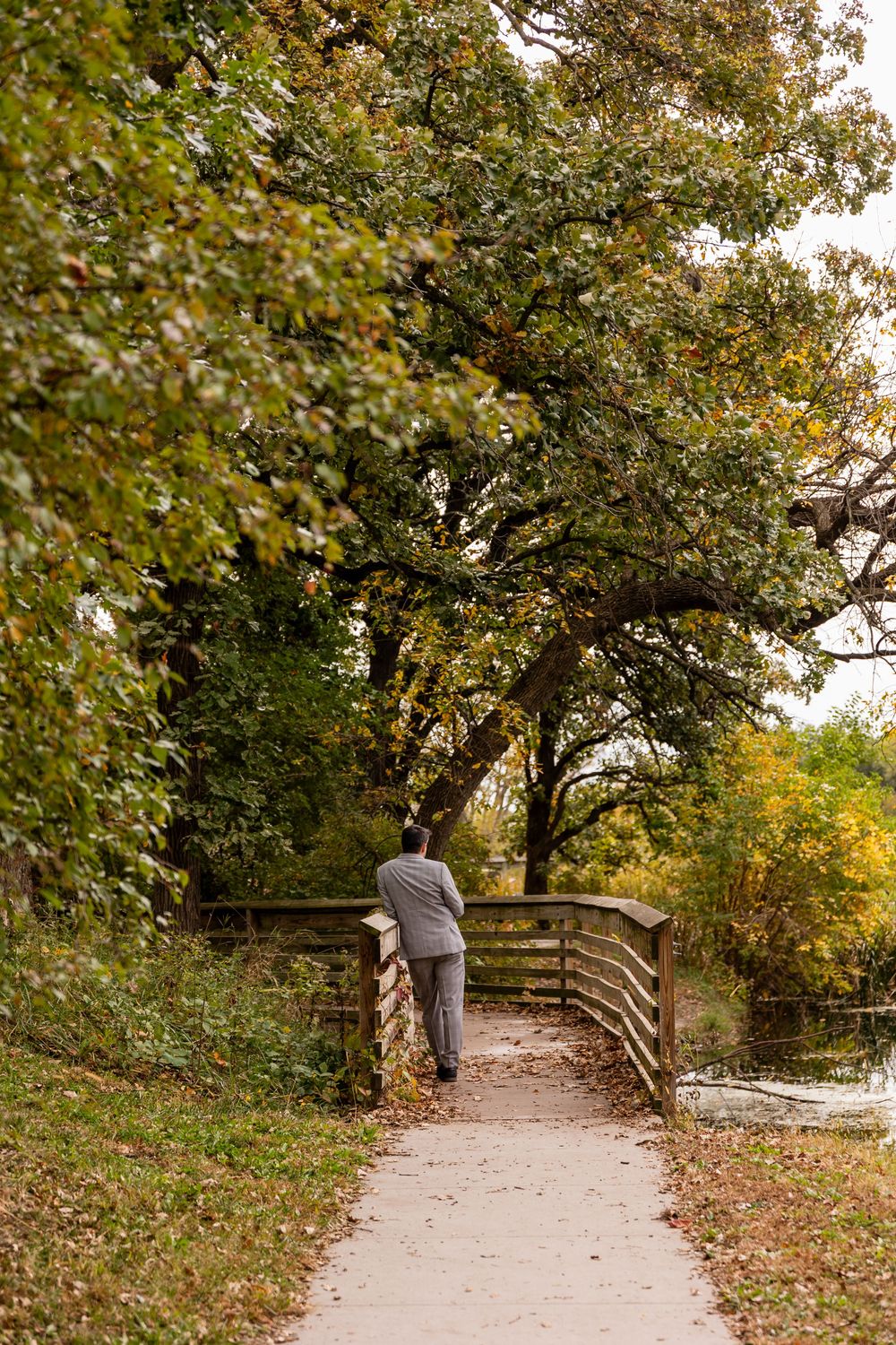 Groom standing on a wooden bridge surrounded by autumn trees  at Platte River State Park in Louisville, NE