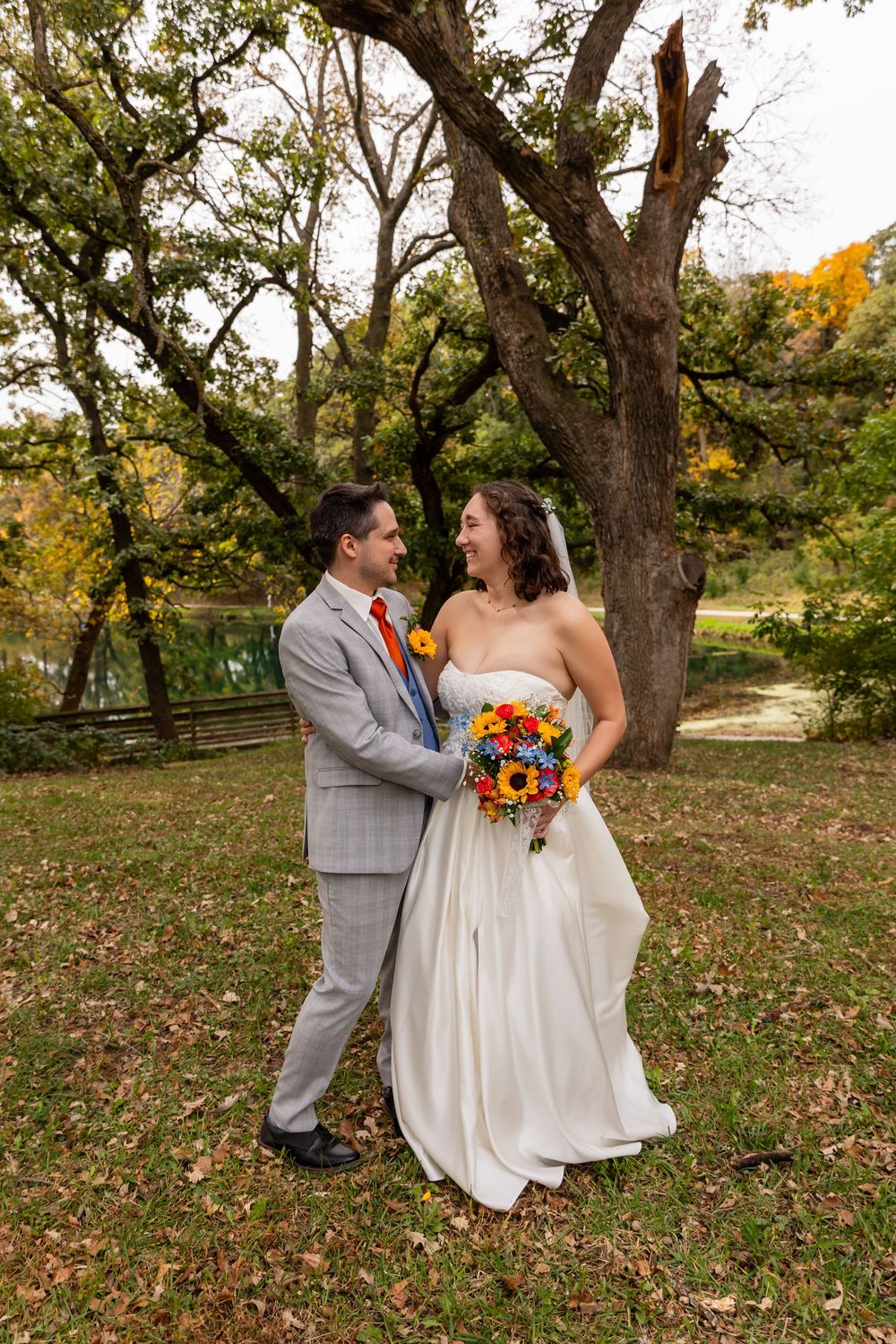 Bride and groom share a joyful moment outdoors among fall foliage, bride holding vibrant sunflower bouquet at Platte River State Park