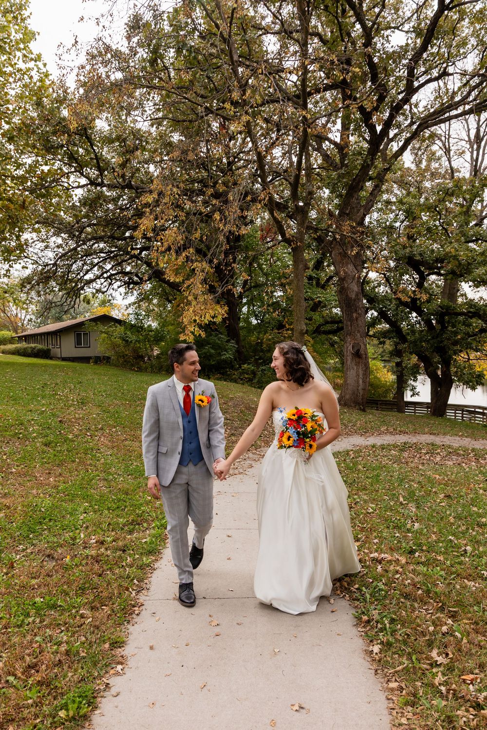 Bride and groom holding hands walking on a path with fall foliage at Platte River State Park in Louisville, NE