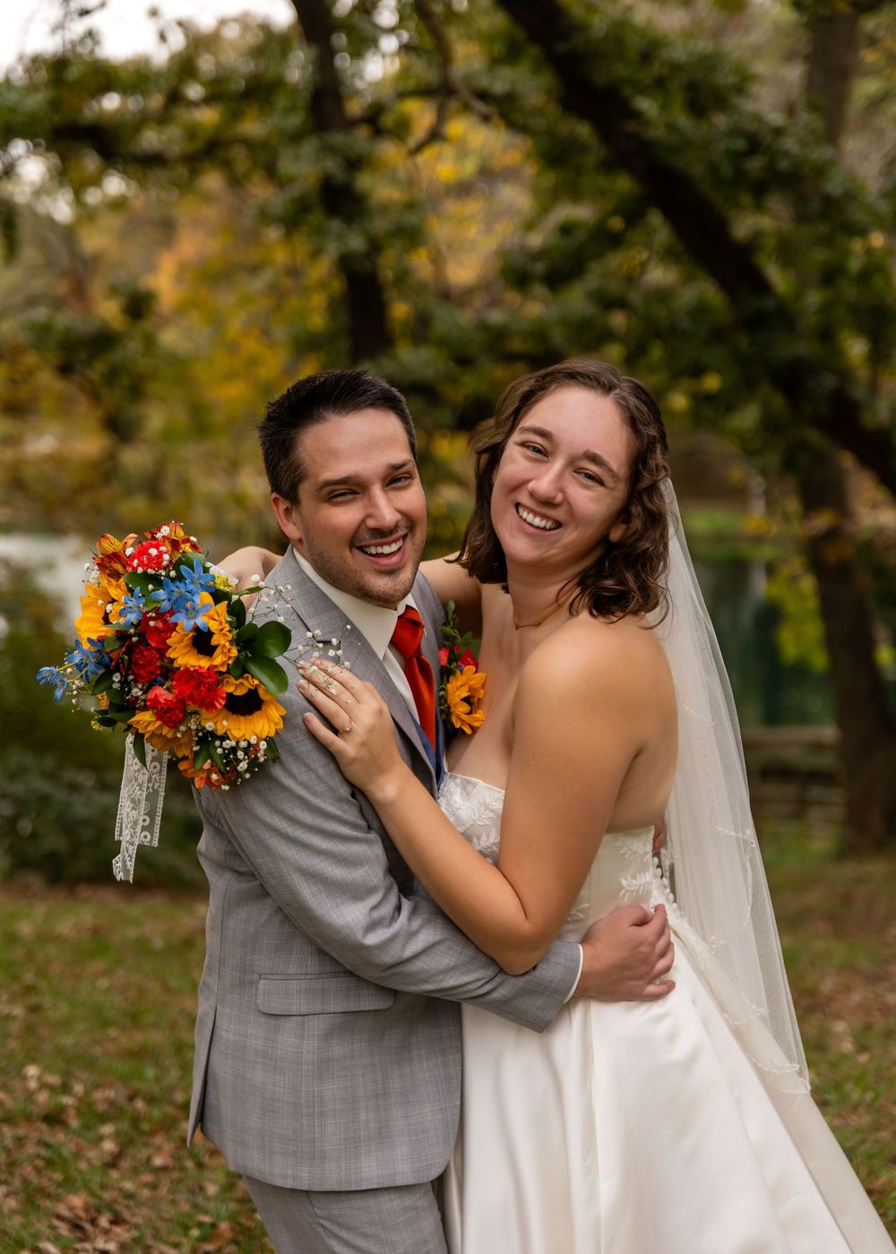 Smiling bride and groom embrace outdoors holding colorful sunflower bouquet during fall wedding portrait at Platte River State Park