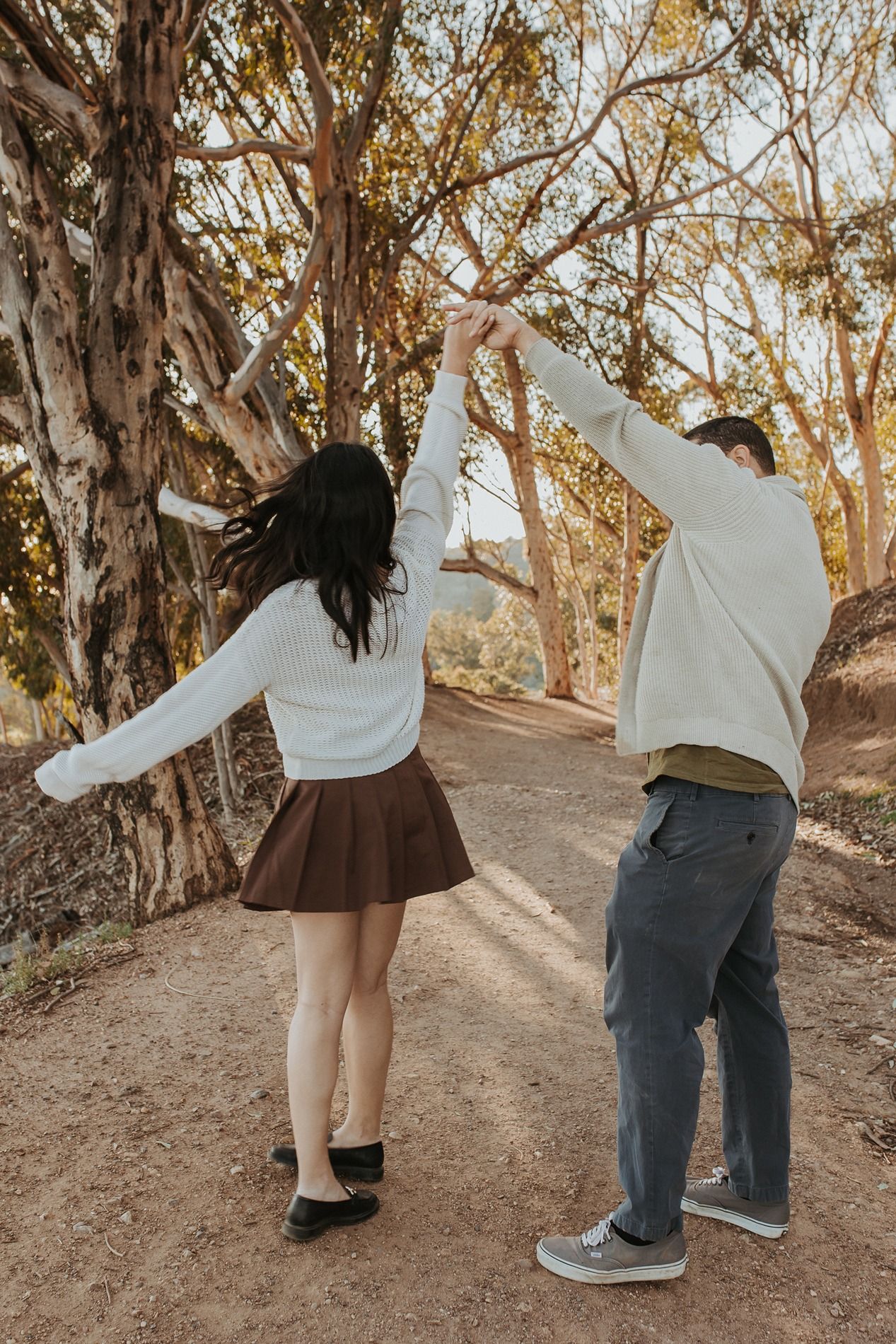 A couple spins and dances together on a dirt trail through eucalyptus trees at sunset at Will Rogers State Park.