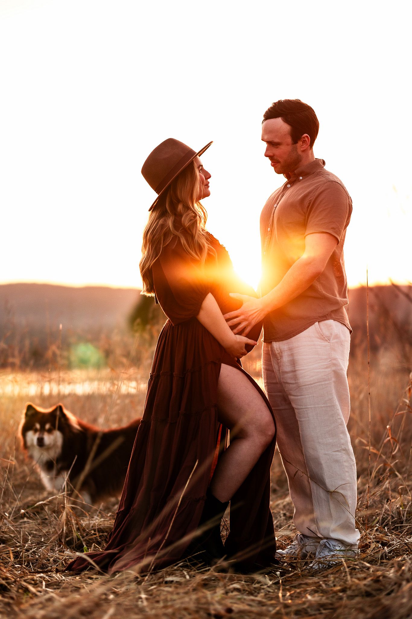 Romantic couple embracing in golden sunlight during sunset photoshoot in a field.