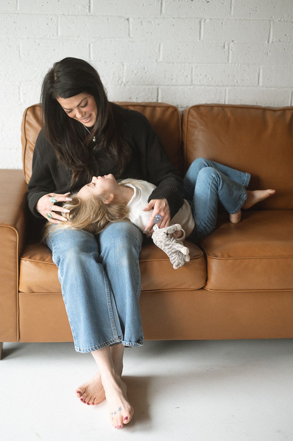 Person relaxing on a brown leather couch in casual clothing while playing with a small white cat.