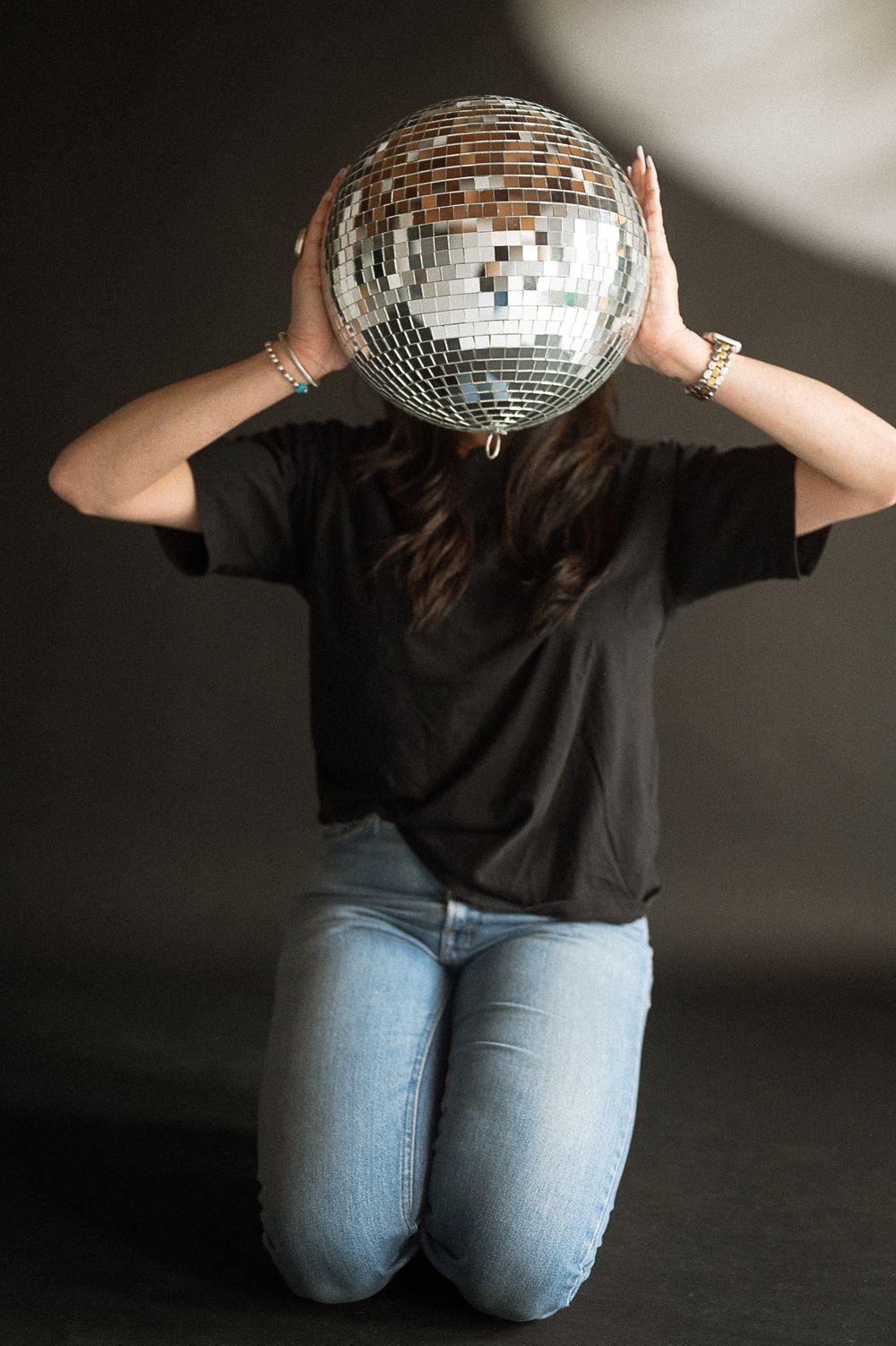 Person wearing black t-shirt and jeans holds disco ball in front of face in artistic photo sequence.