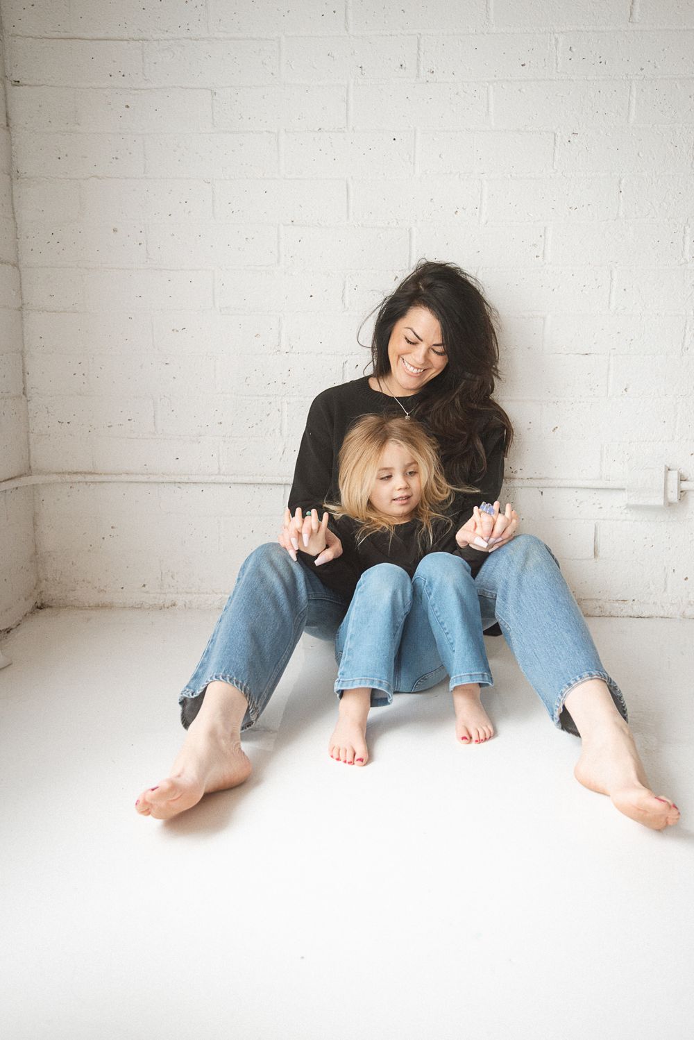 Two people in denim and black tops lounging casually on white floor showing bare feet.