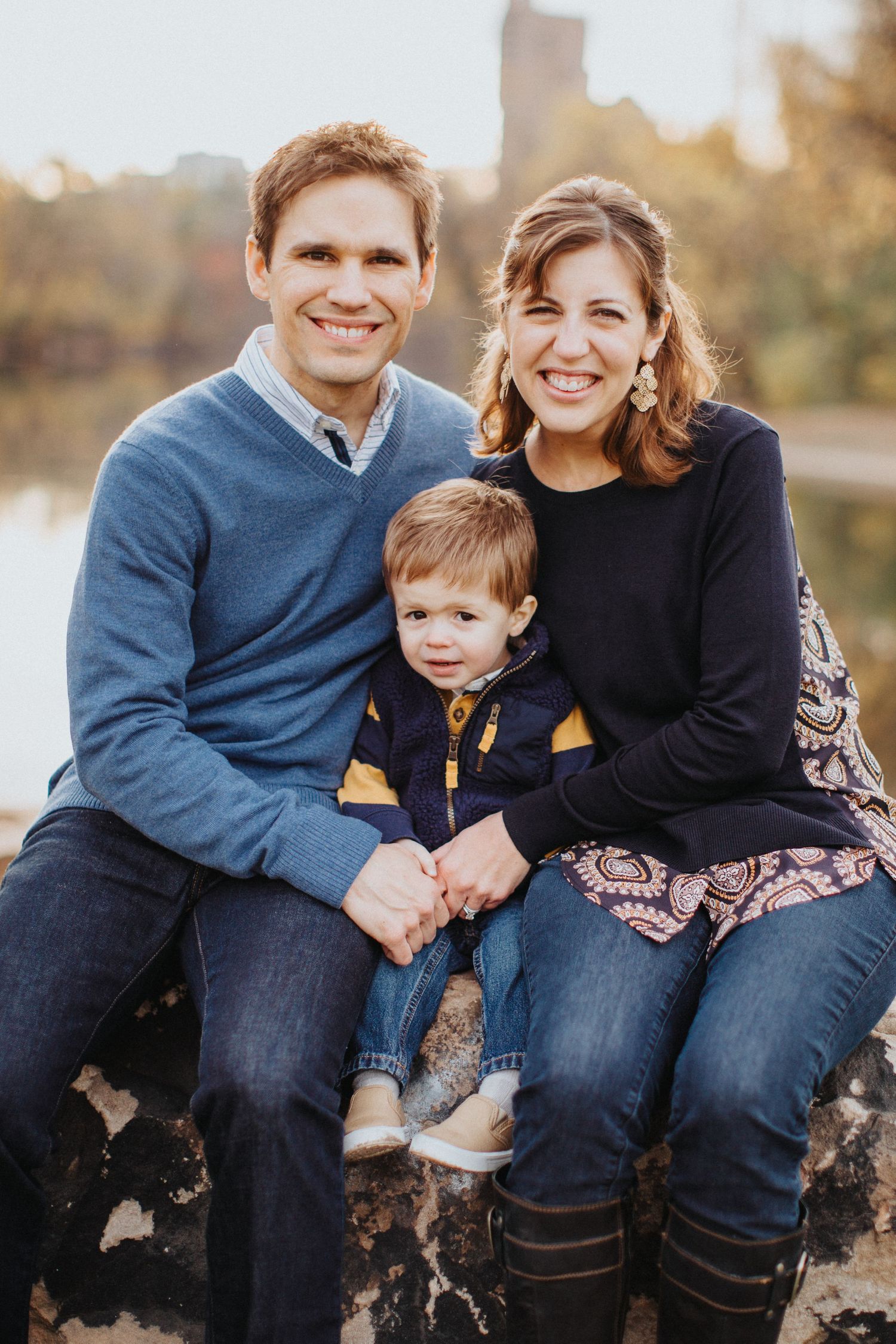 Outdoor family portrait at sunset in a park with fall foliage in the background.
