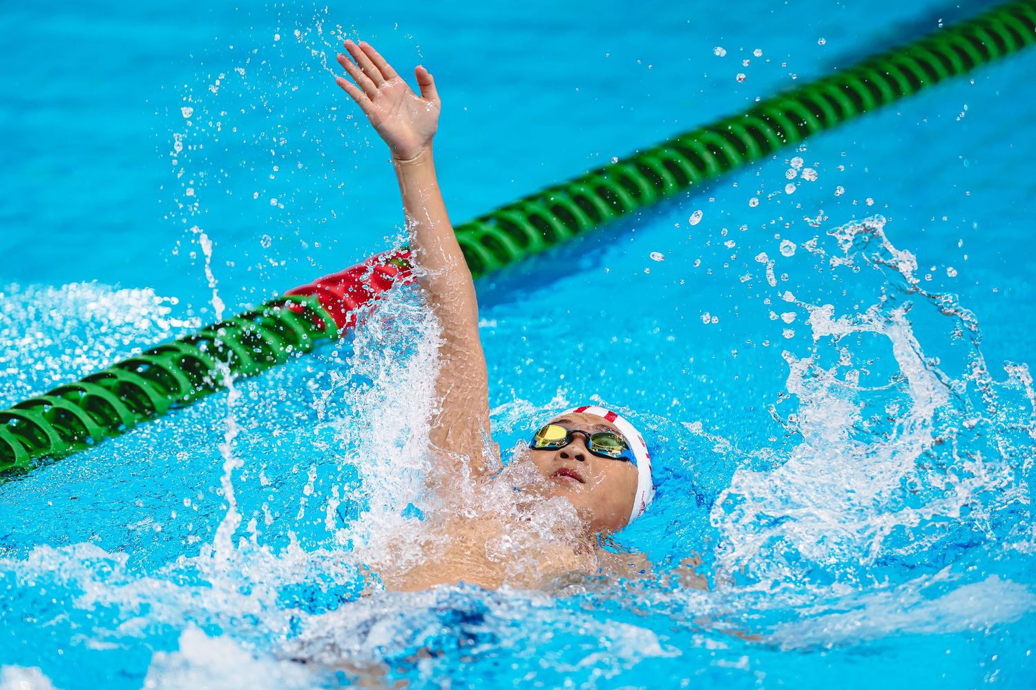 Swimmer performing butterfly stroke in a competition pool with lane lines visible in bright blue water.