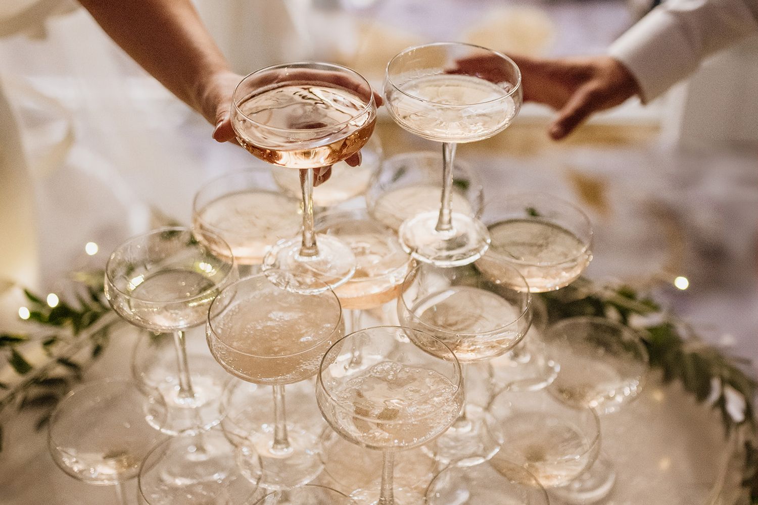 Champagne tower with glasses being filled at an elegant celebration, bride and groom holding glass.
