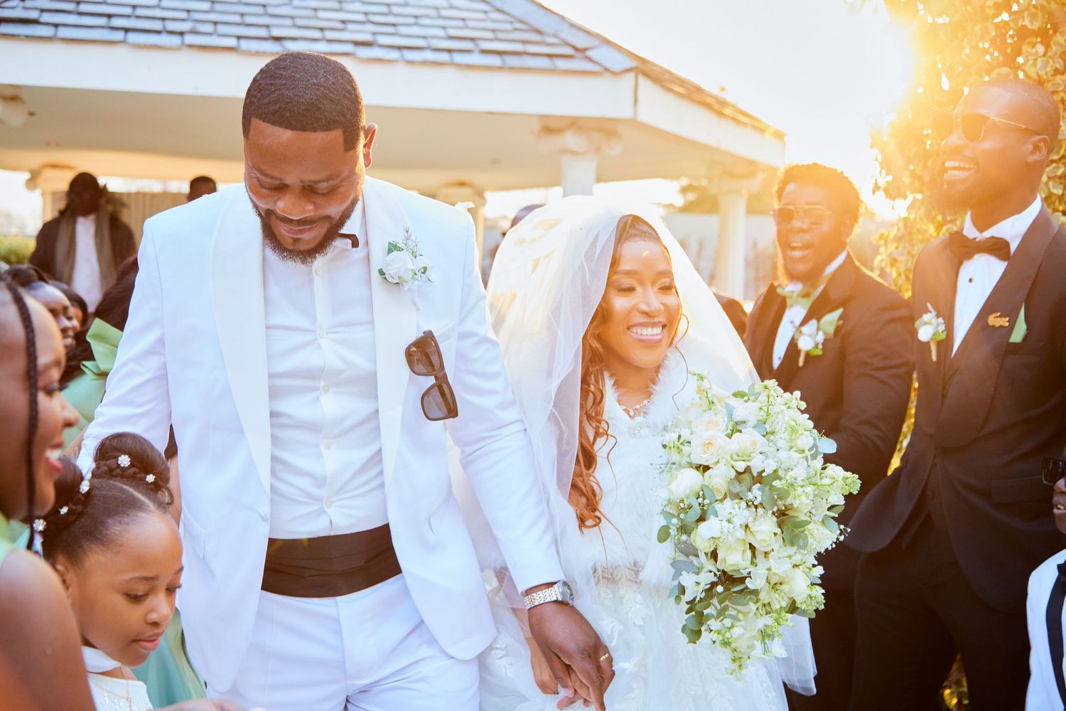 A joyful wedding party celebrates outdoors during golden hour.