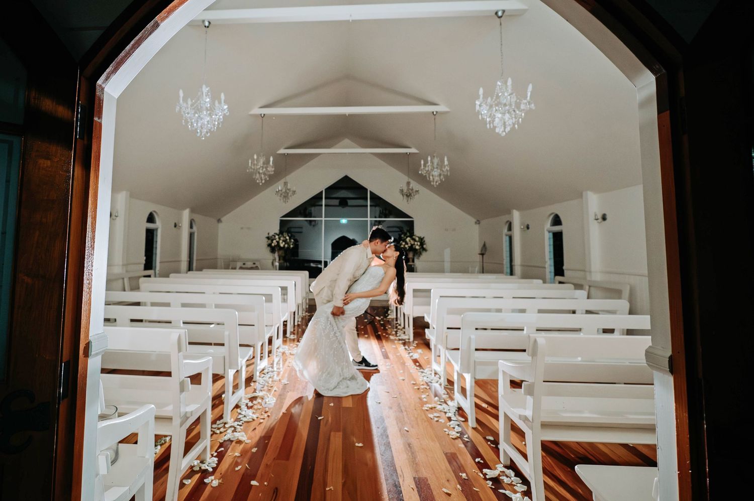 Inside view of an elegant white chapel with crystal chandeliers and wooden pews creating a perfect wedding aisle.