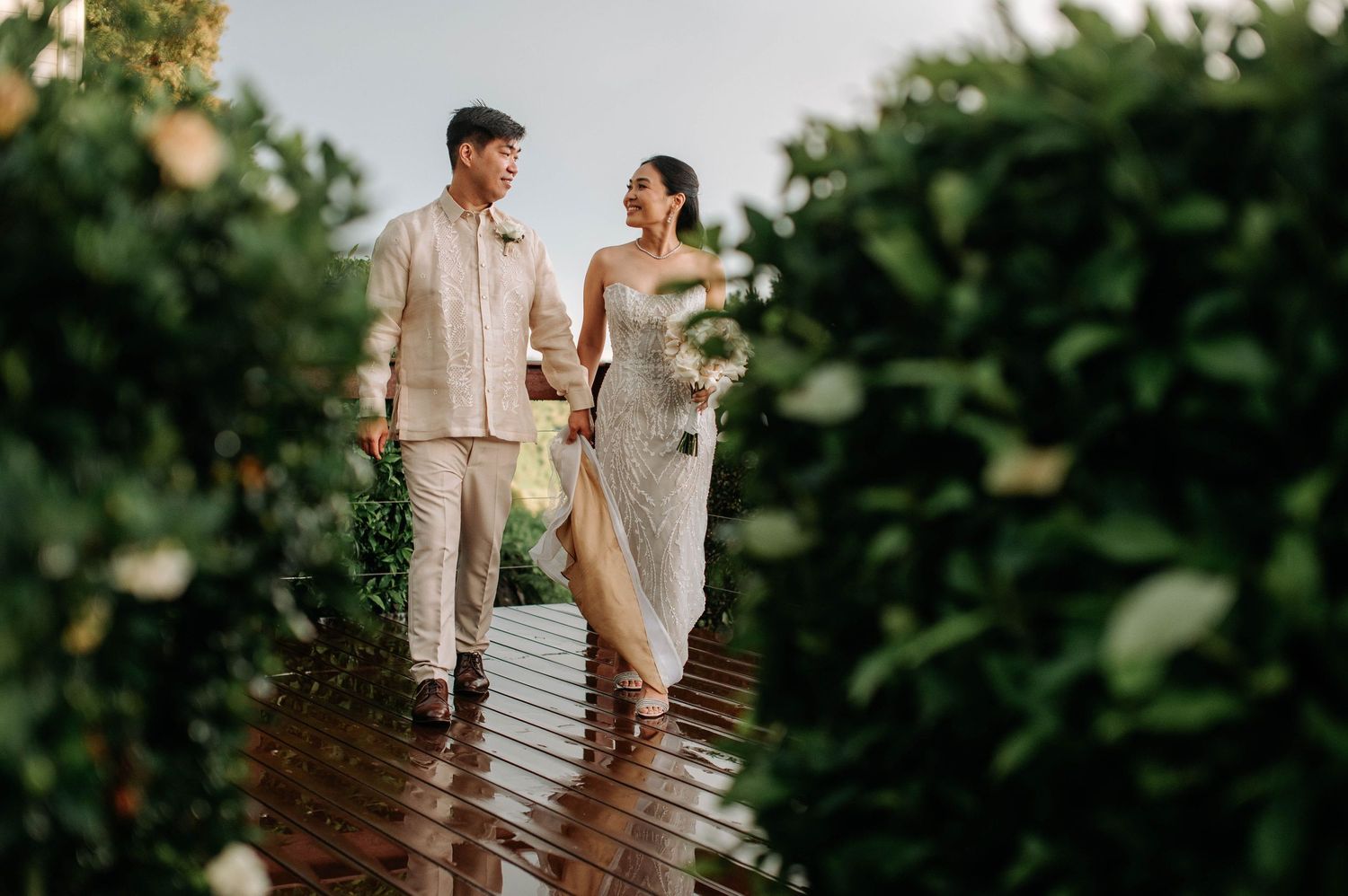 Couple walking hand in hand on rainy wooden deck during outdoor wedding photoshoot.