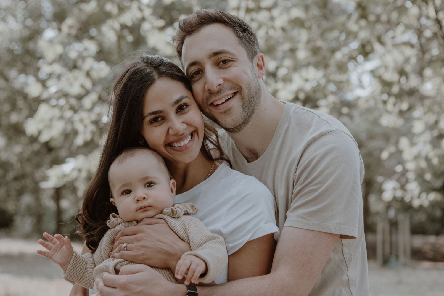 Intimate family portrait showing tender moment with baby against blooming spring trees.