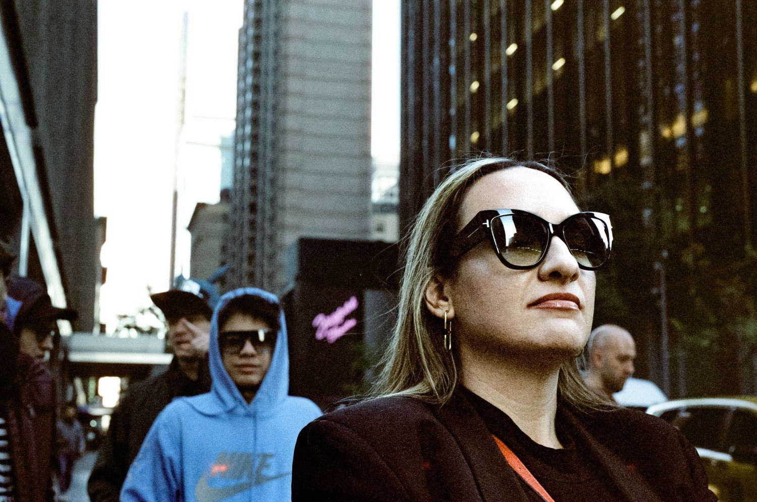 Urban street fashion portrait with sunglasses and city buildings in background.