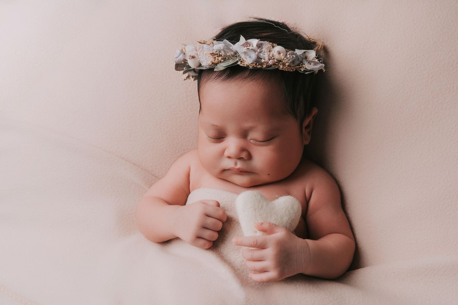 A sweet newborn baby lying on a soft pink blanket in a minimalist studio setting.