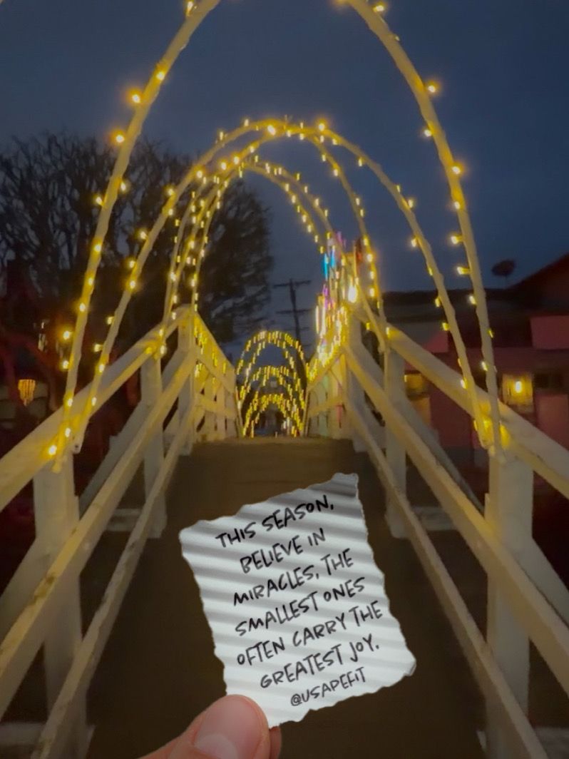 A hand holds a paper note against a backdrop of illuminated arches with warm glowing lights at dusk.
