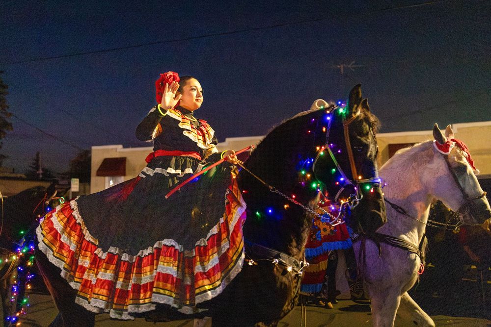Colorful holiday lights illuminate performers during a nighttime street parade celebration.