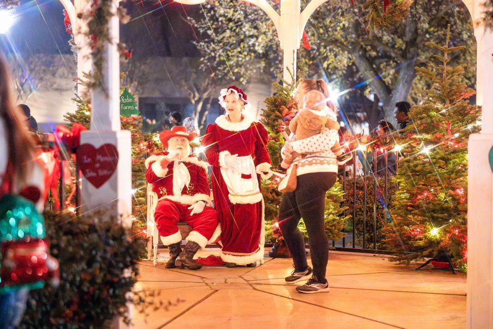Festive outdoor holiday display with Santa Claus figures and twinkling lights creating a magical Christmas scene.