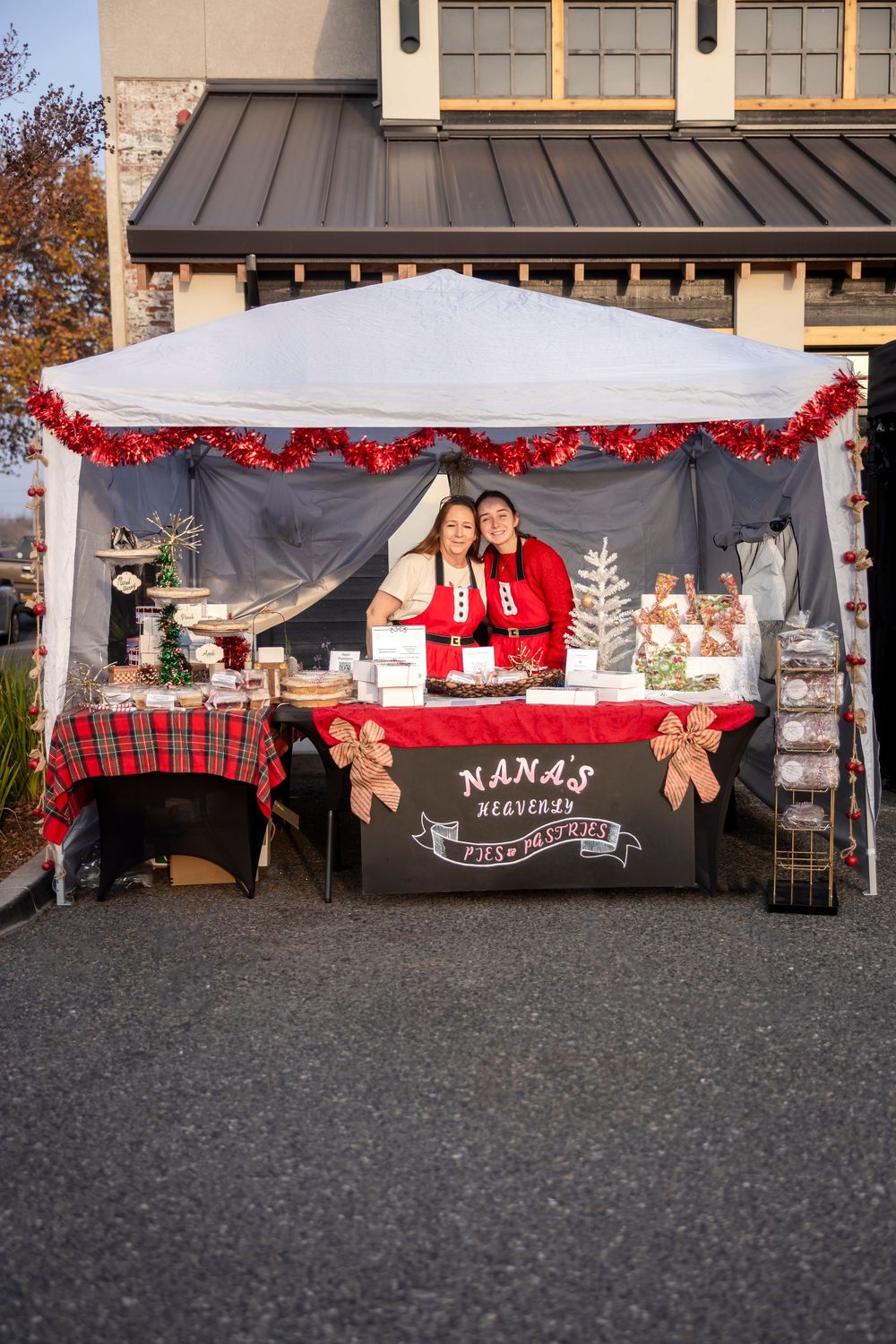 A festive holiday market booth decorated with red and plaid accents displays treats and Christmas decor under a white tent.