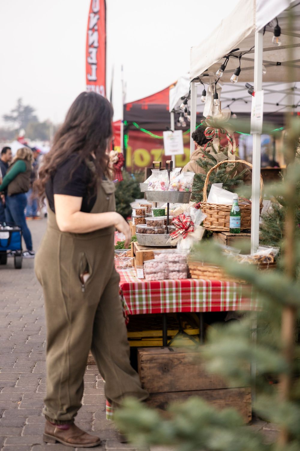 A shopper browses items at an outdoor market stall with checkered tablecloths and displayed merchandise.