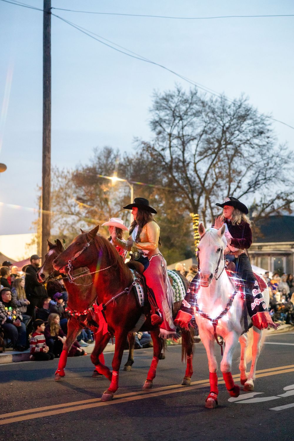 People in festive red costumes perform a choreographed dance routine at a holiday parade during dusk.