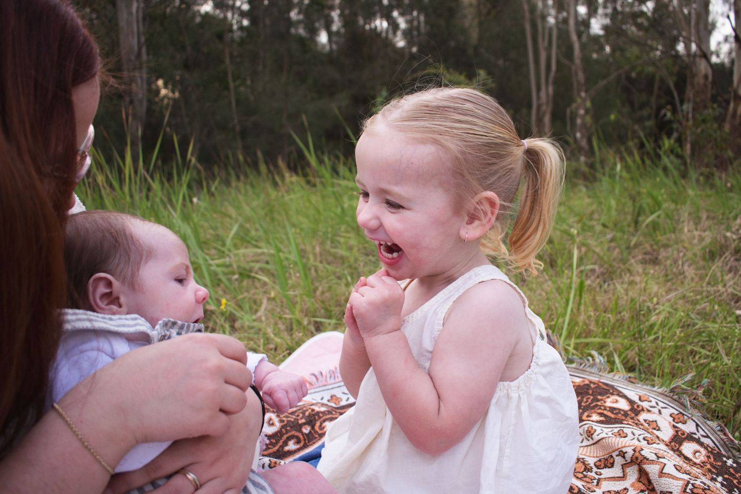 Toddler laughing as she plays with her mum and newborn baby brother during a golden hour bush countryside newborn photoshoot in Maitland NSW