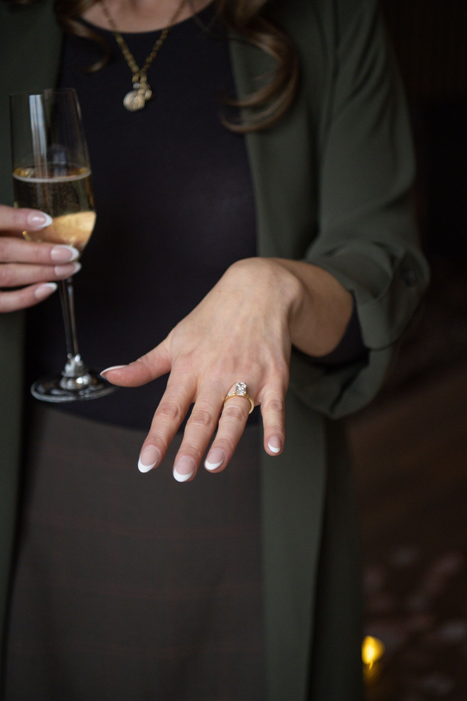Close-up of hands holding champagne glasses and showing an engagement ring.