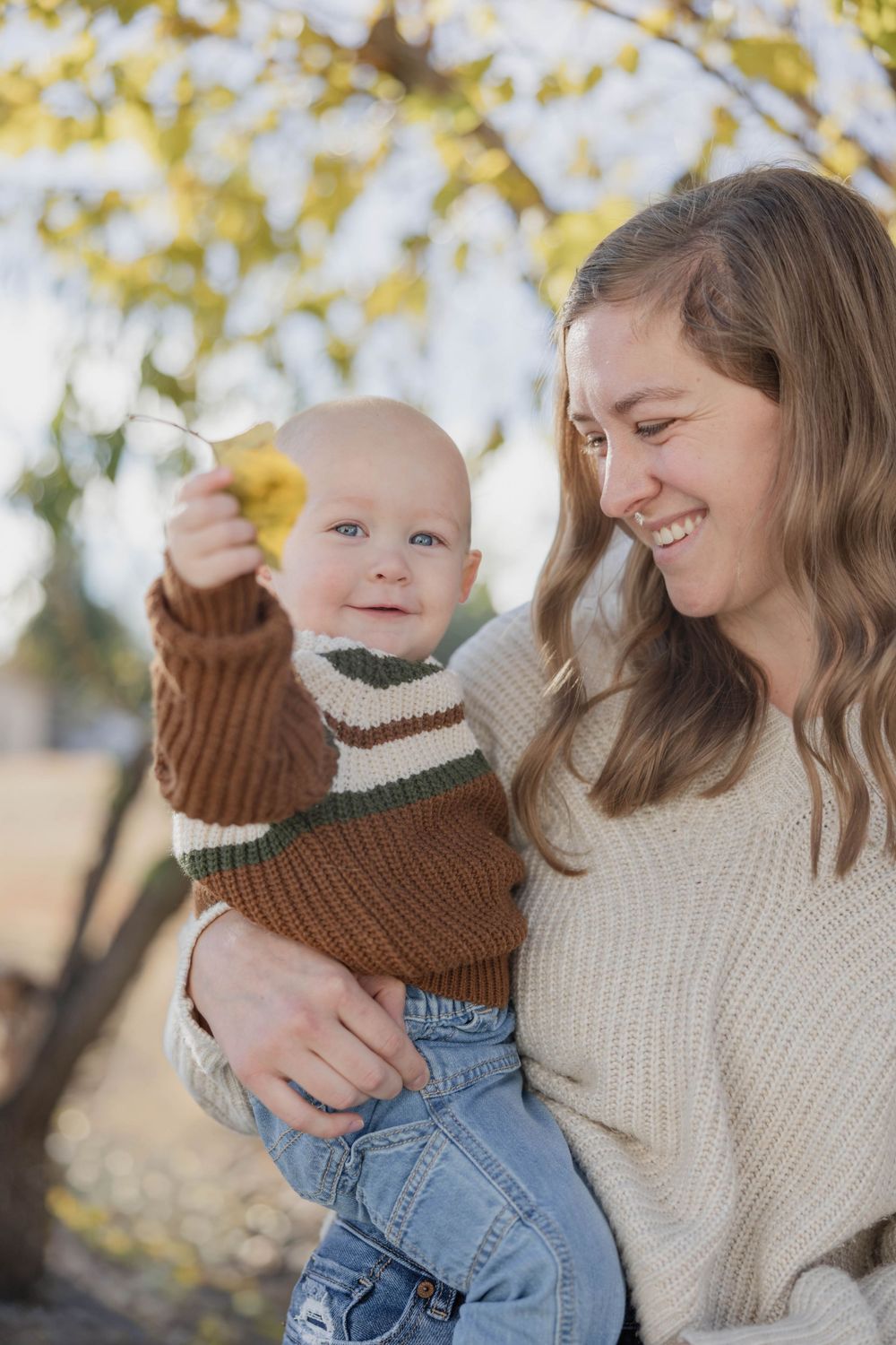 Parent and child share playful moment under yellow autumn leaves.