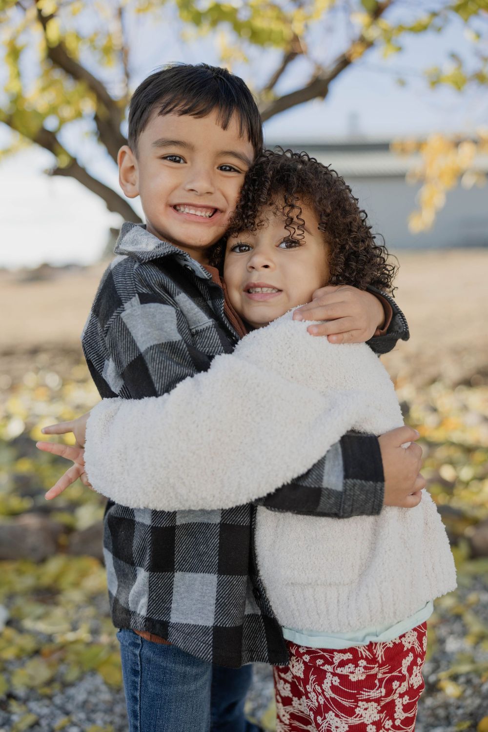 Two children hugging and smiling during outdoor autumn photoshoot.