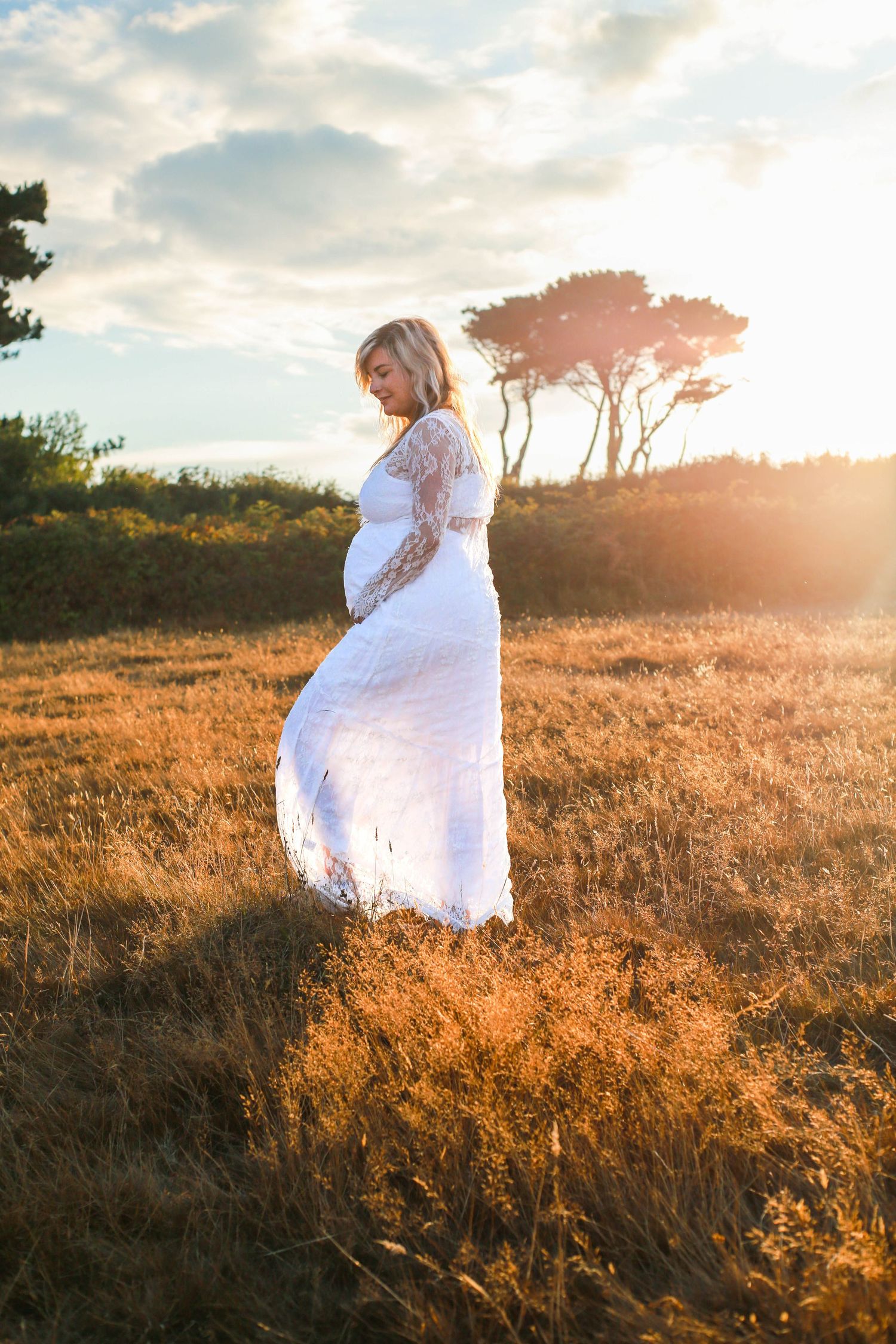 A figure in a flowing white dress walks through a golden field at sunset creating an ethereal silhouette.