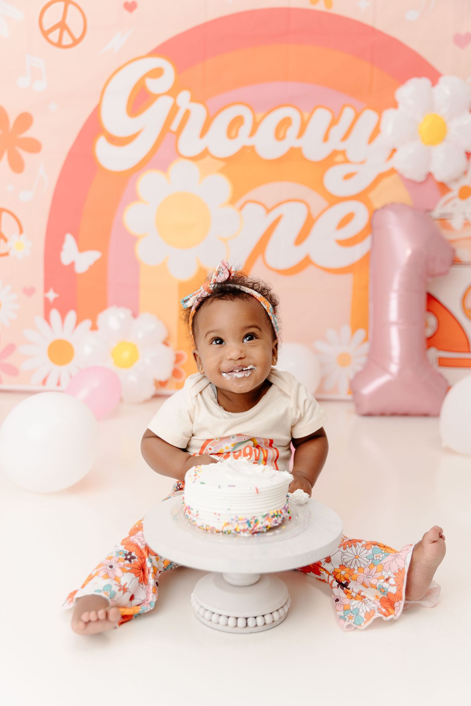 First birthday cake smash photo session with rainbow backdrop, flowers and pink decorations.