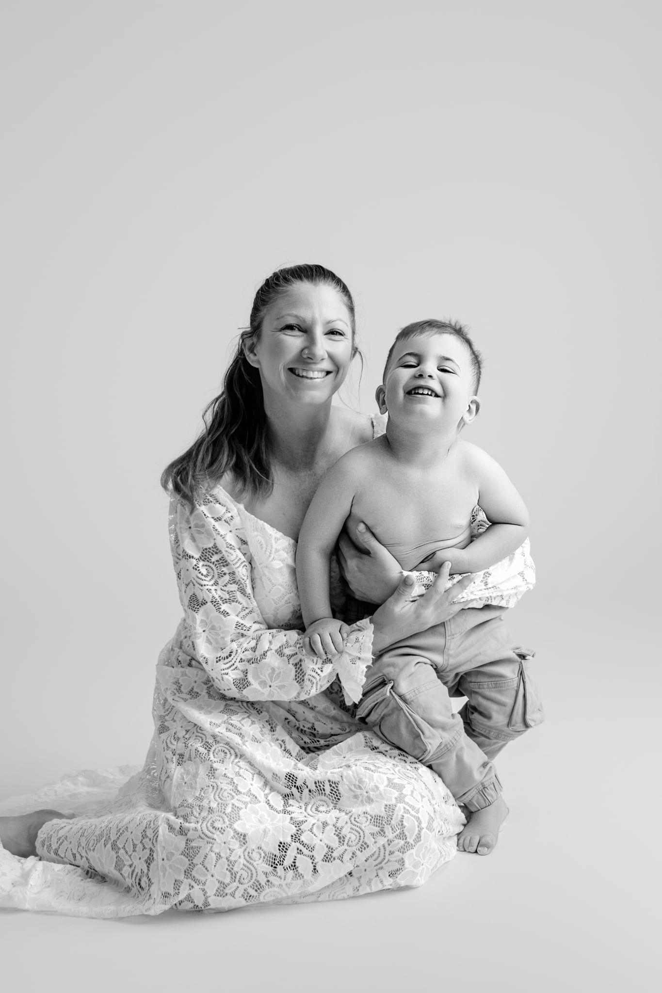 A tender moment captured in a series of photos showing a parent in a white lace dress holding a baby against a gray backdrop.