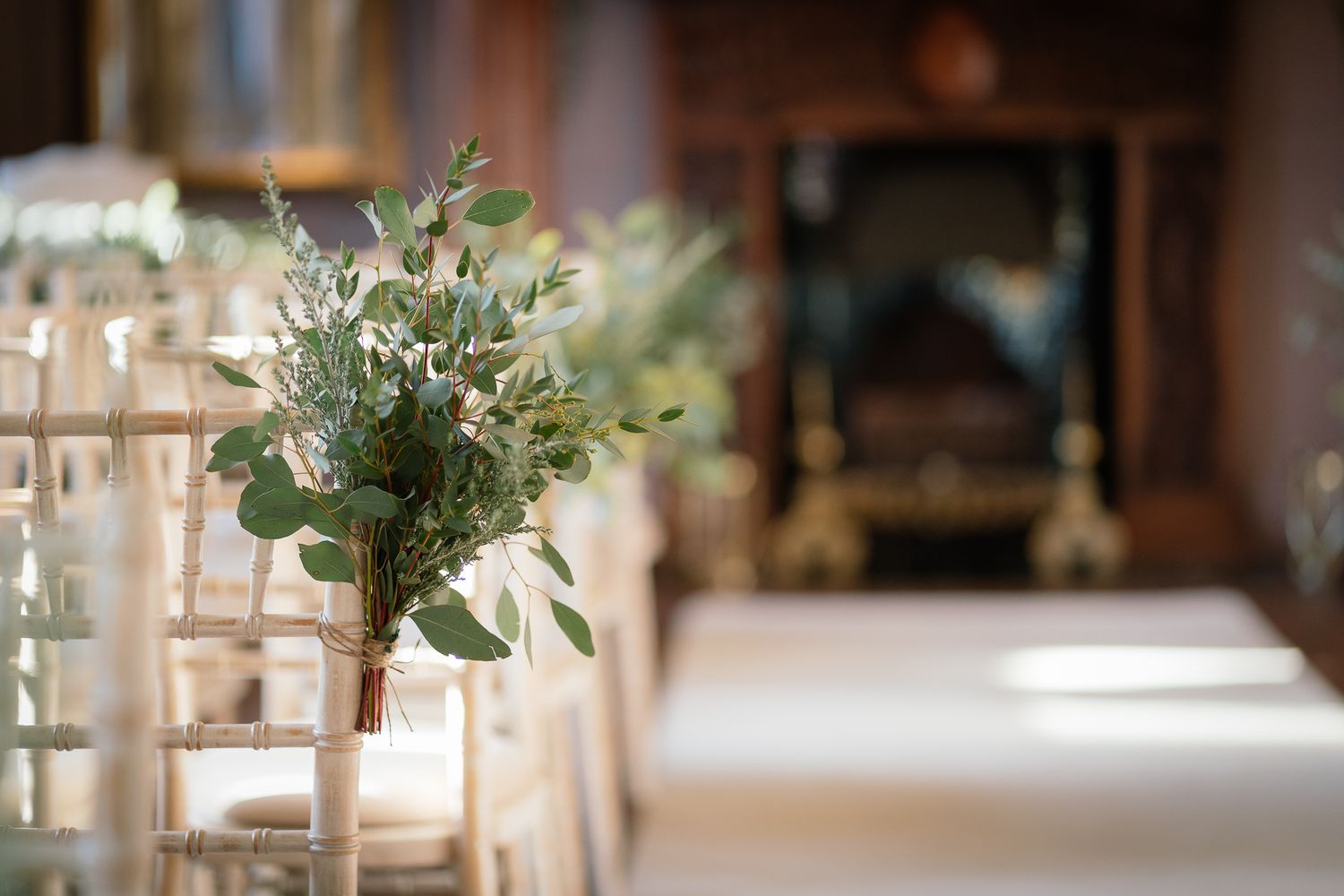 Delicate floral arrangements with eucalyptus and white flowers line the ceremony aisle. Ellingham Hall