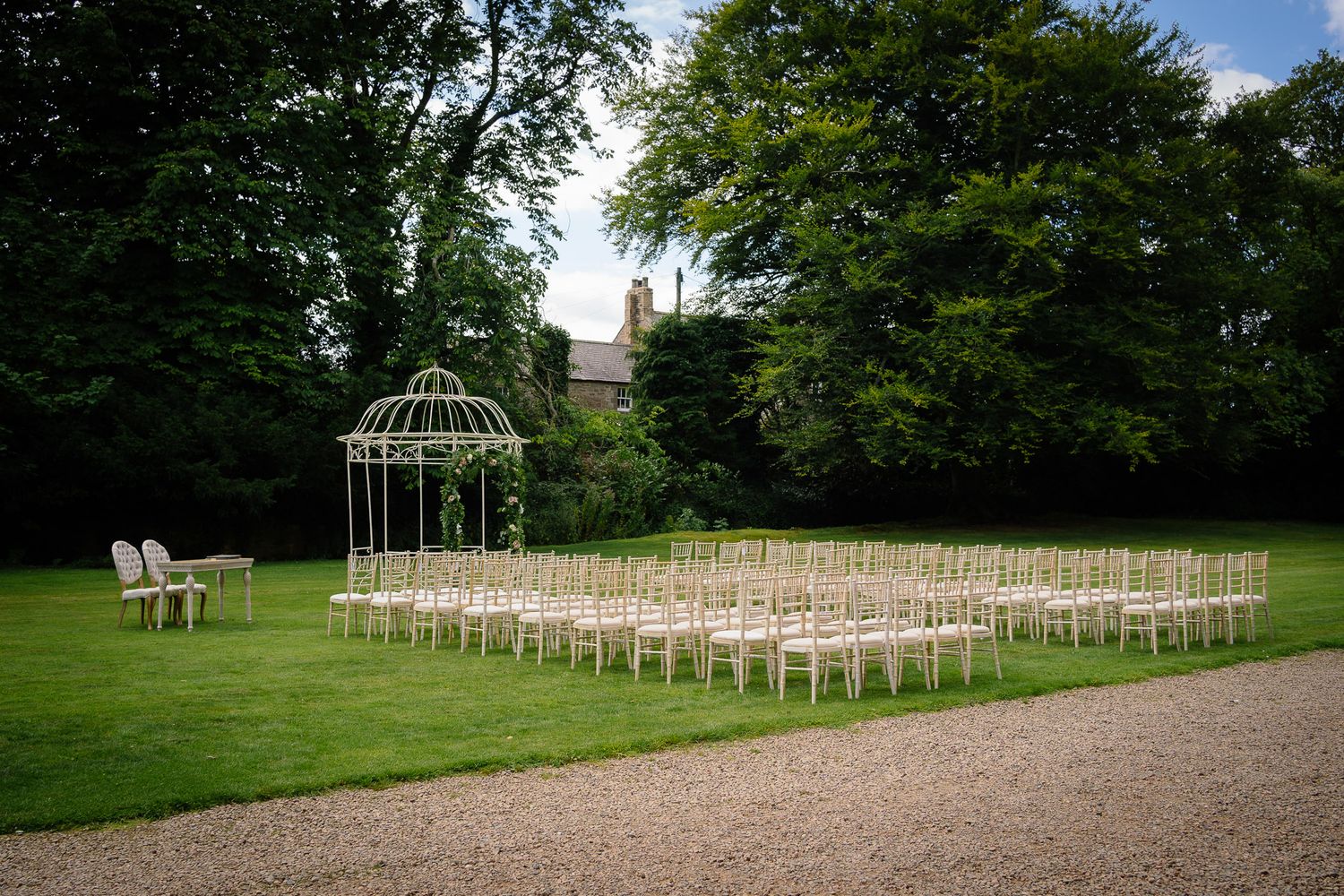White garden chairs arranged in neat rows on a manicured lawn with a decorative gazebo. Ellingham Hall