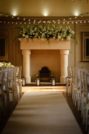 Indoor wedding ceremony space with white chairs and romantic string light decorations overhead. Ellingham Hall