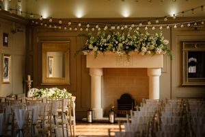 Elegant wedding venue hall with string lights and white chairs arranged in rows for a ceremony. Ellingham Hall