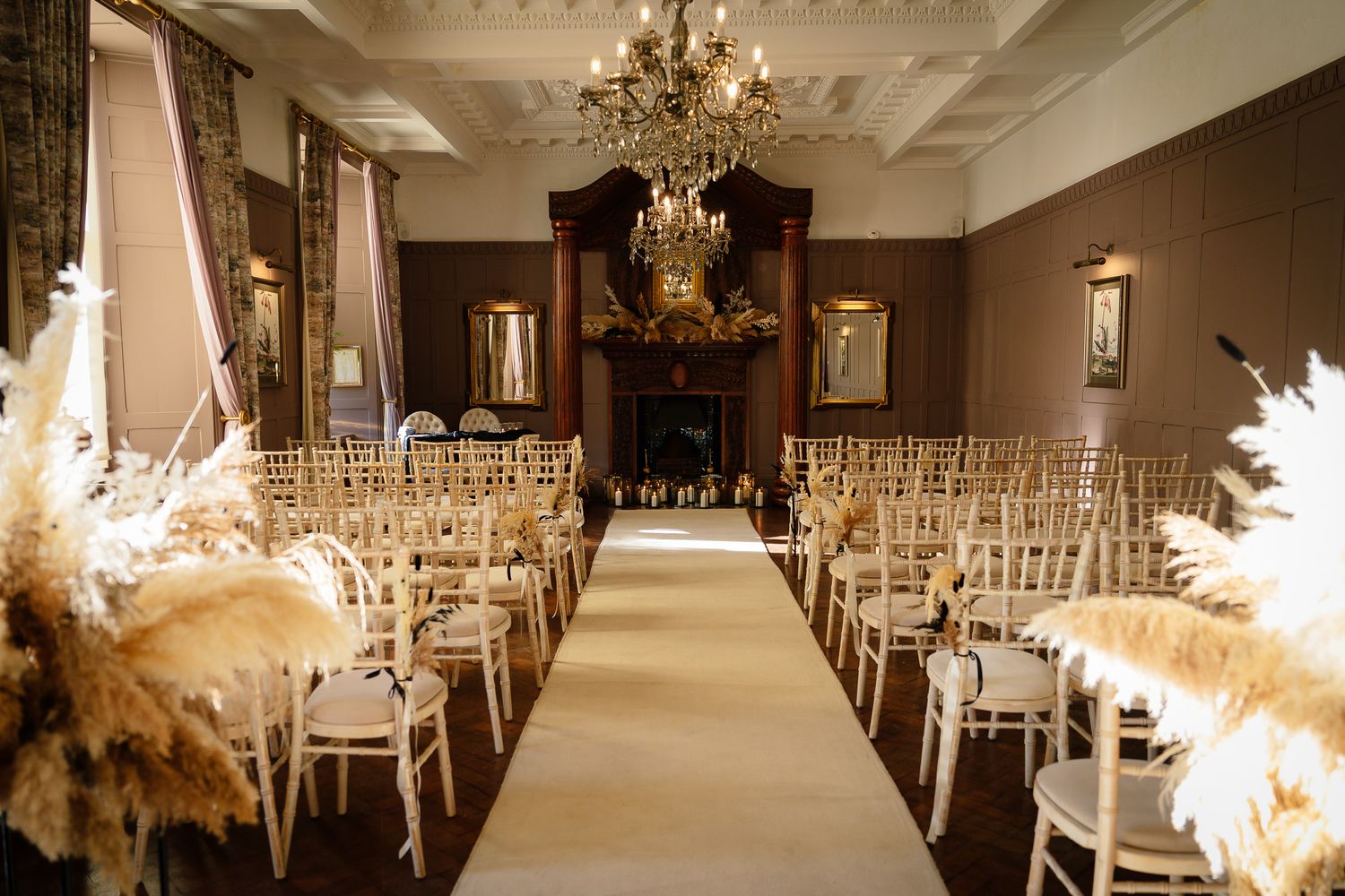 Luxurious indoor wedding venue with crystal chandeliers and white chiavari chairs arranged for ceremony. Ellingham Hall