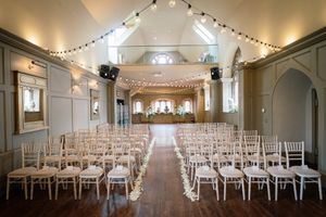 Panoramic view of a chapel interior with string lights and white chairs set up for a wedding ceremony. Ellingham Hall