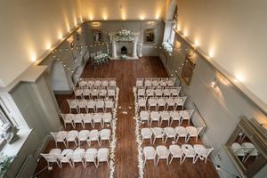 White chairs arranged in rows for a wedding ceremony in an elegant indoor venue with warm lighting and high ceilings. Ellingham Hall