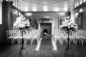 Black and white photo of an empty reception venue with string lights and white chairs. Ellingham Hall