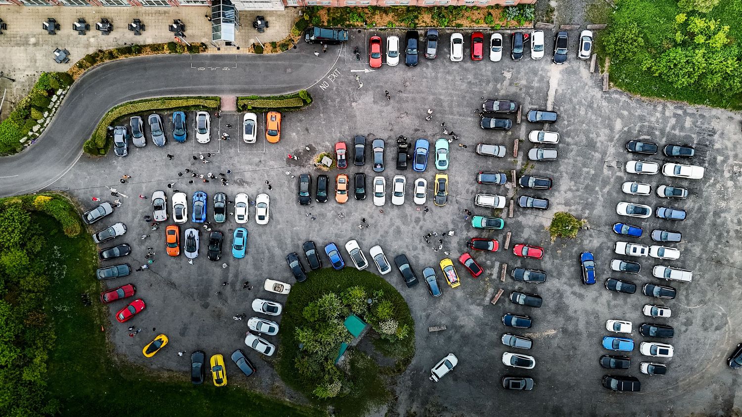 Bird's eye view of parking lot filled with various vehicles and green spaces.