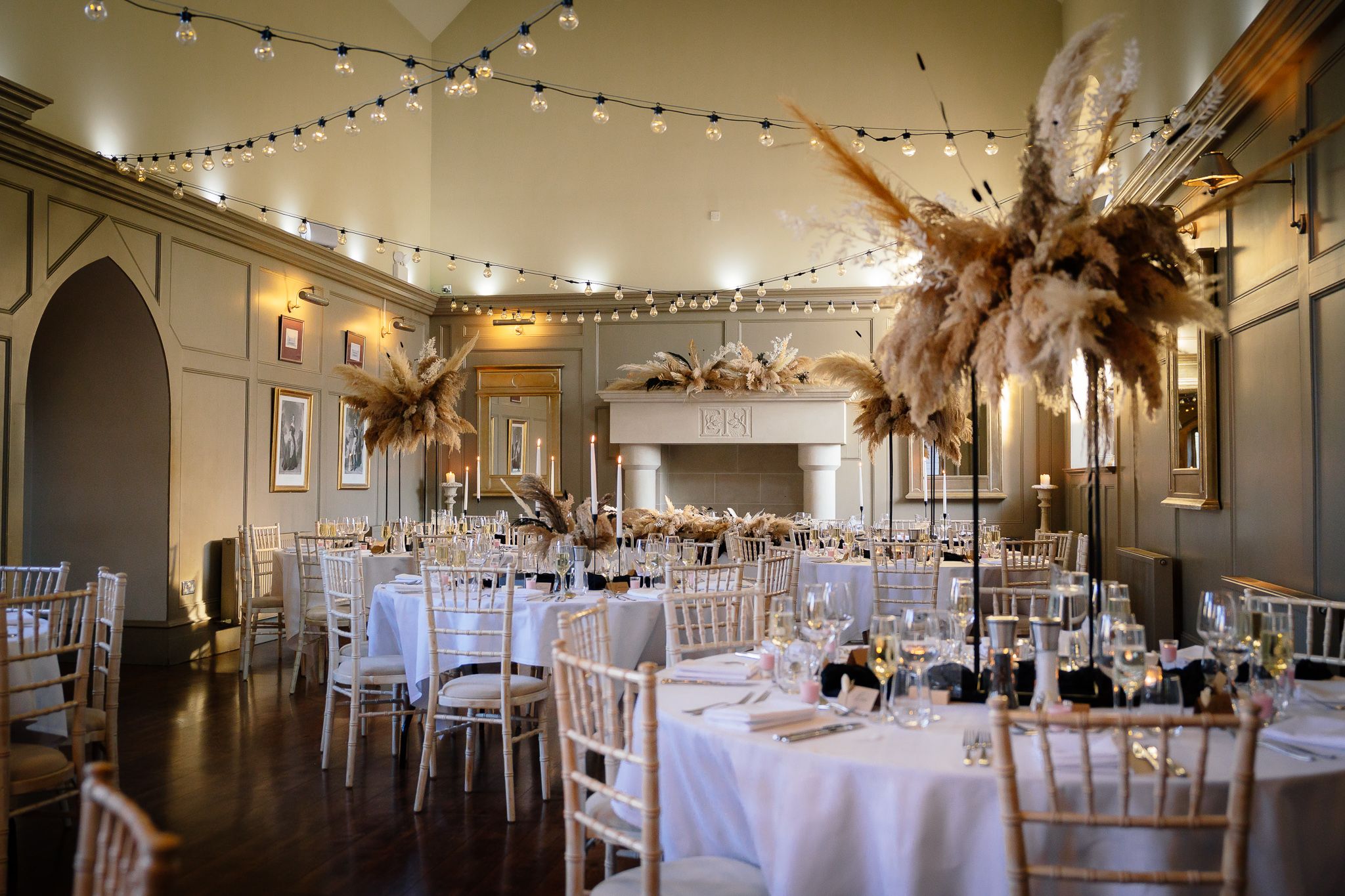 Panoramic view of an elegant reception hall with string lights and white tablecloths. Ellingham Hall