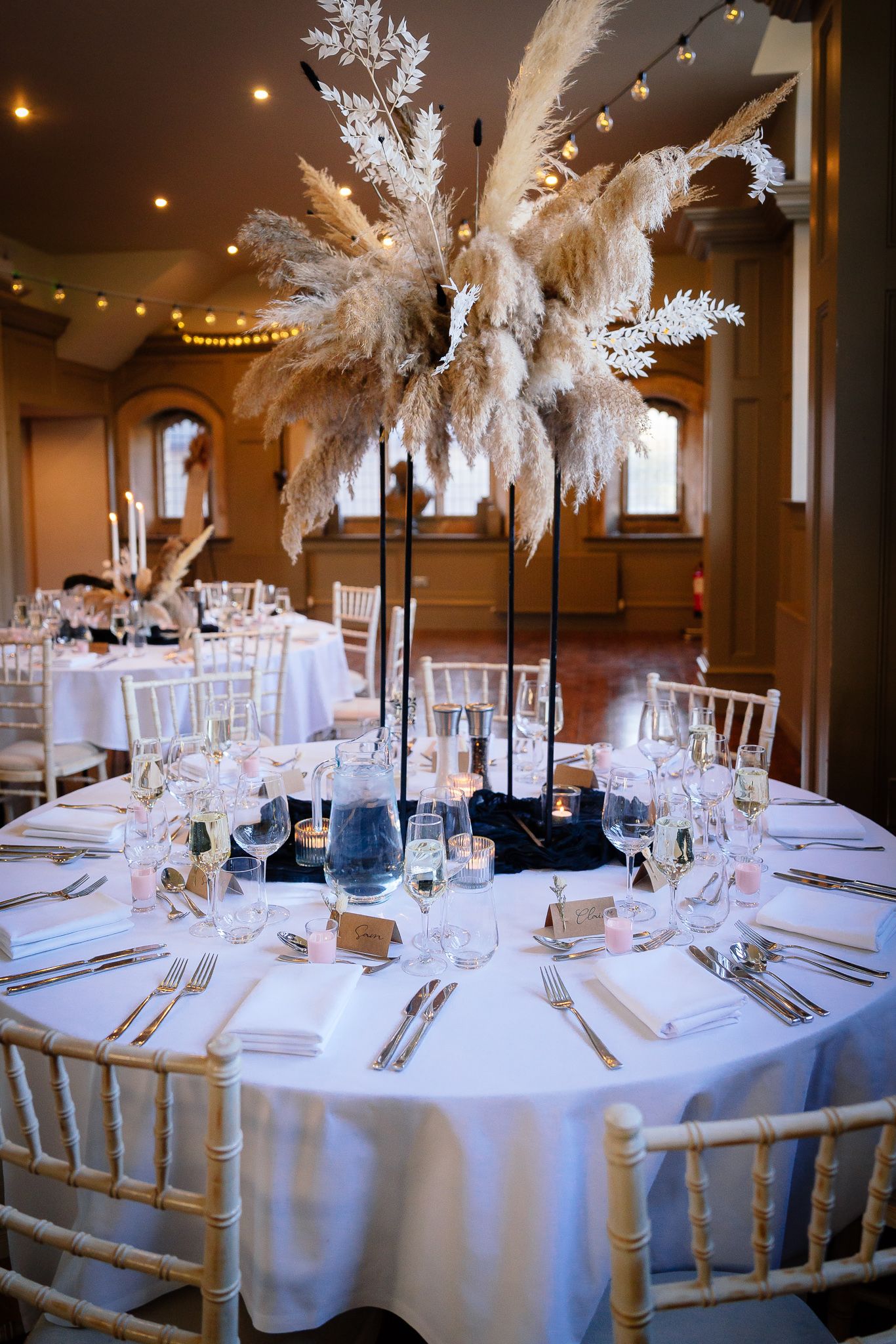 White feather centerpieces adorn round tables at an elegant wedding reception. Ellingham Hall