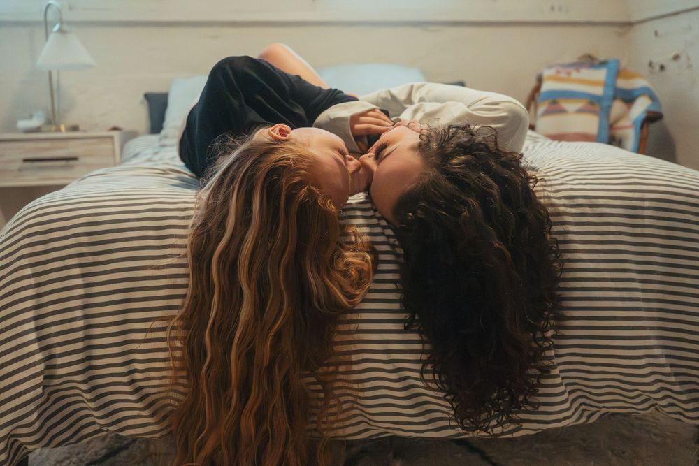 Two people with long hair lying close together on striped bedding.